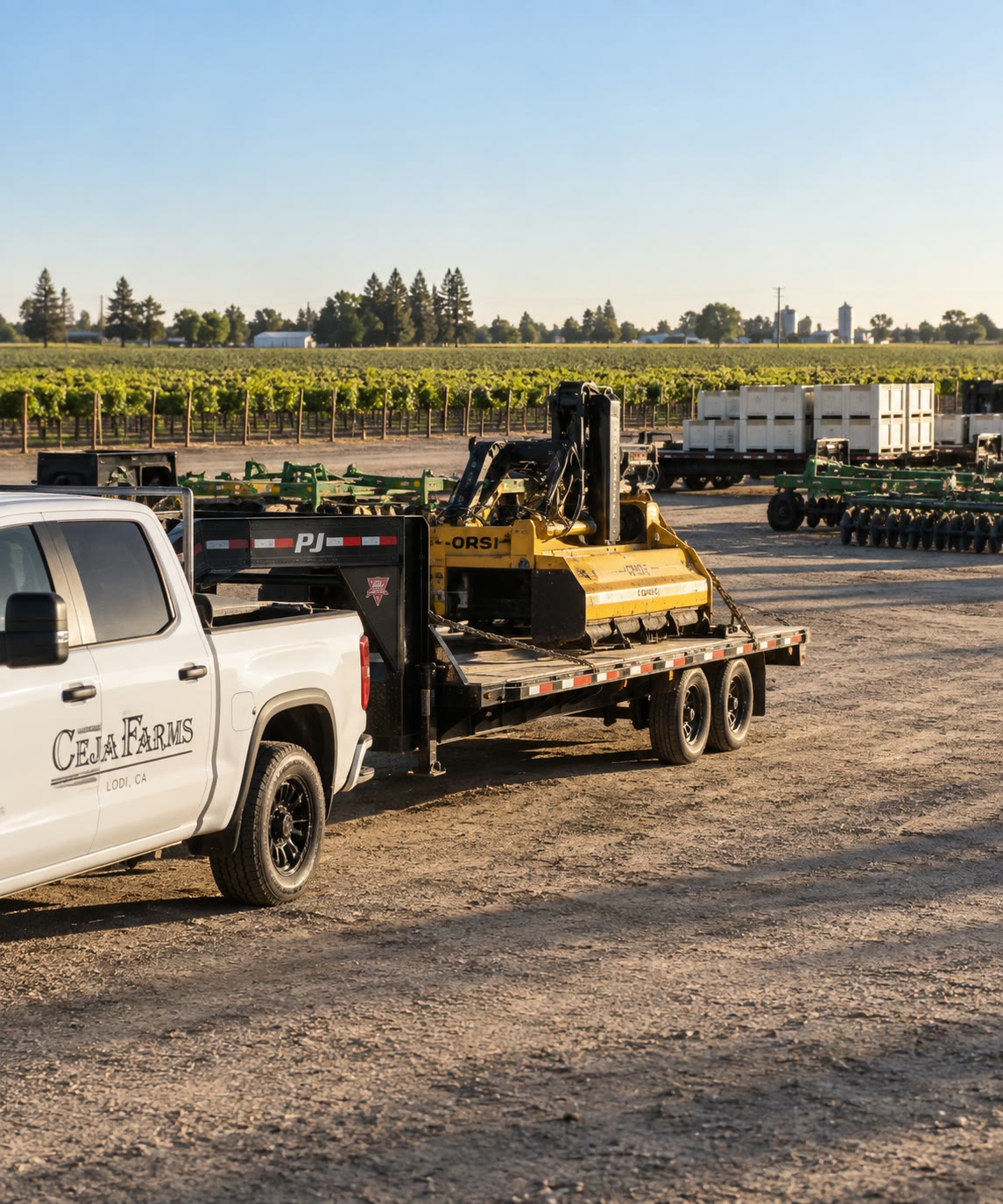Ceja Farms pickup towing a flatbed trailer loaded with a flail mower past disc harrows and harvest bins